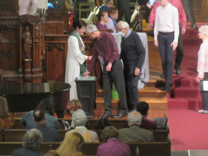 At the front of a church, people line up before a minister in white robes to 