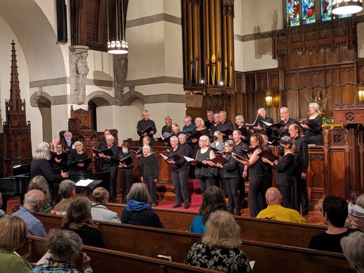 A large choir, all dressed in black, hold songbooks and sing at the front of the Sanctuary.