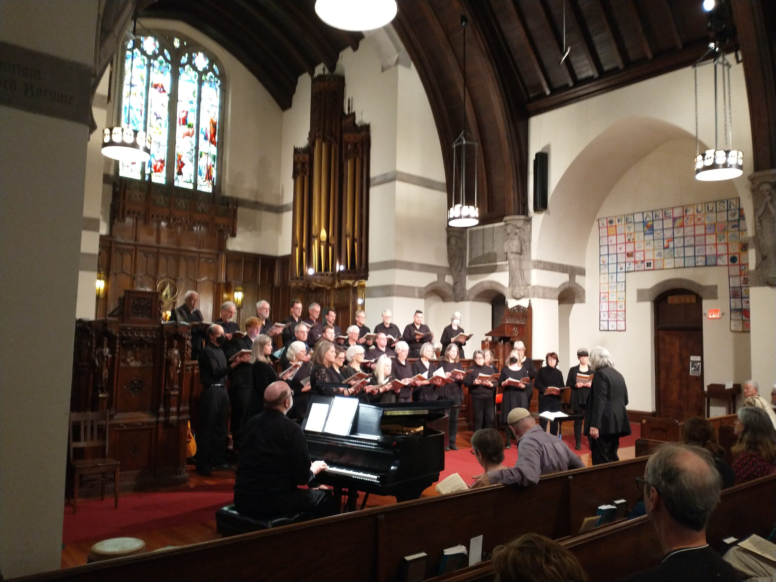 A large choir, dressed in black, sings from the front of the sanctuary, accompanied by a male pianist and directed by a gray-haired woman dressed.