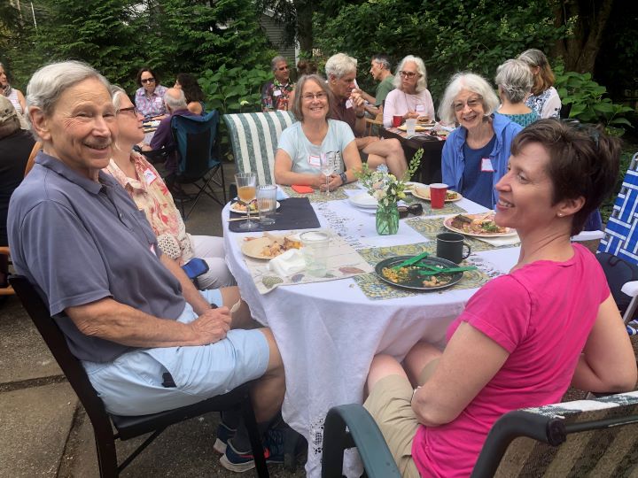 Many adults sit at outdoor tables enjoying a plant-based meal together.