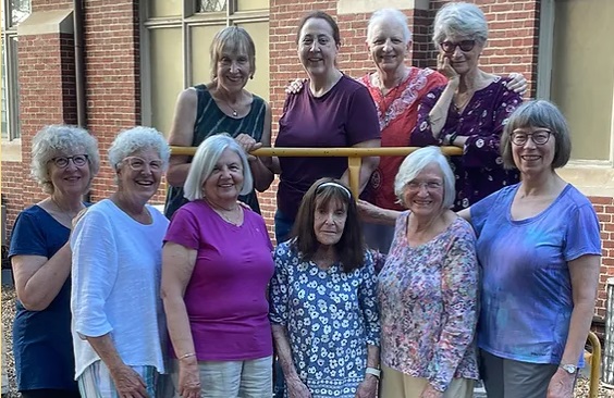 Ten women stand at the entrance to a brick building, six at ground level, and four above them on an entrance landing.