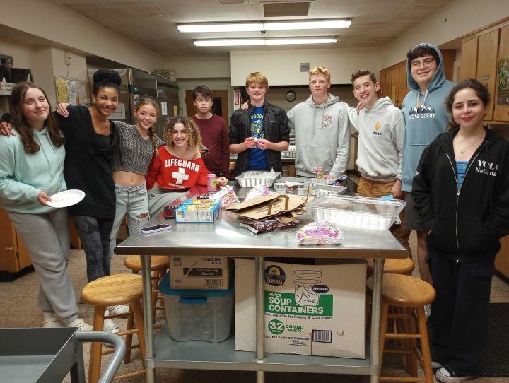 A group of ten youth stand in a large kitchen, cooking together.