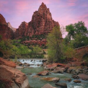 A river flows through the desert as the sun sets behind tall mountain peaks.