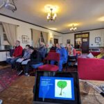 A group of adults seated in a meeting room attend a discussion on climate change and MIT's En-Roads program