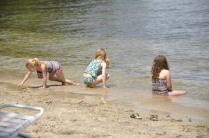 Three children wearing swimsuits play in the water and the sand on a beach at Sandy Island.