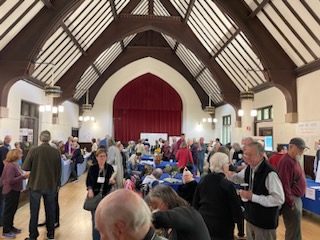 A large function hall with a high vaulted ceiling is filled with people browsing at tables