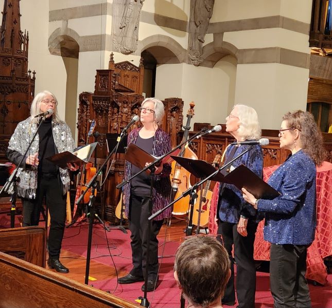 At the front of the Sanctuary, four women holding folders sing into microphones