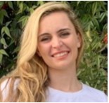 Against a background of summertime greenery, a headshot of a smiling woman with long blonde hair wearing a white blouse.